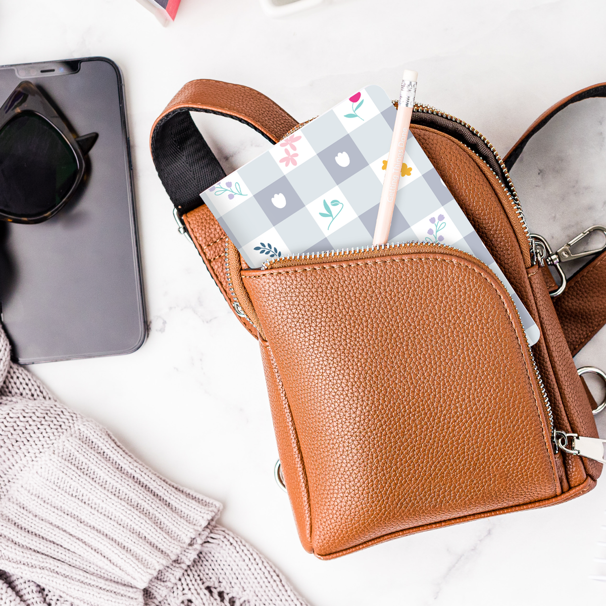 A mockup of the Gingham Floral Mini Notebook and a pencil inside a purse.