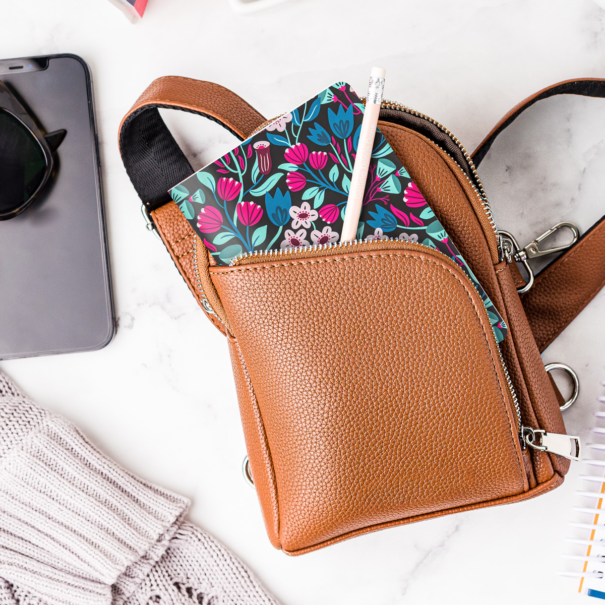 A mockup of the Dark Floral mini notebook and a pencil in a purse.