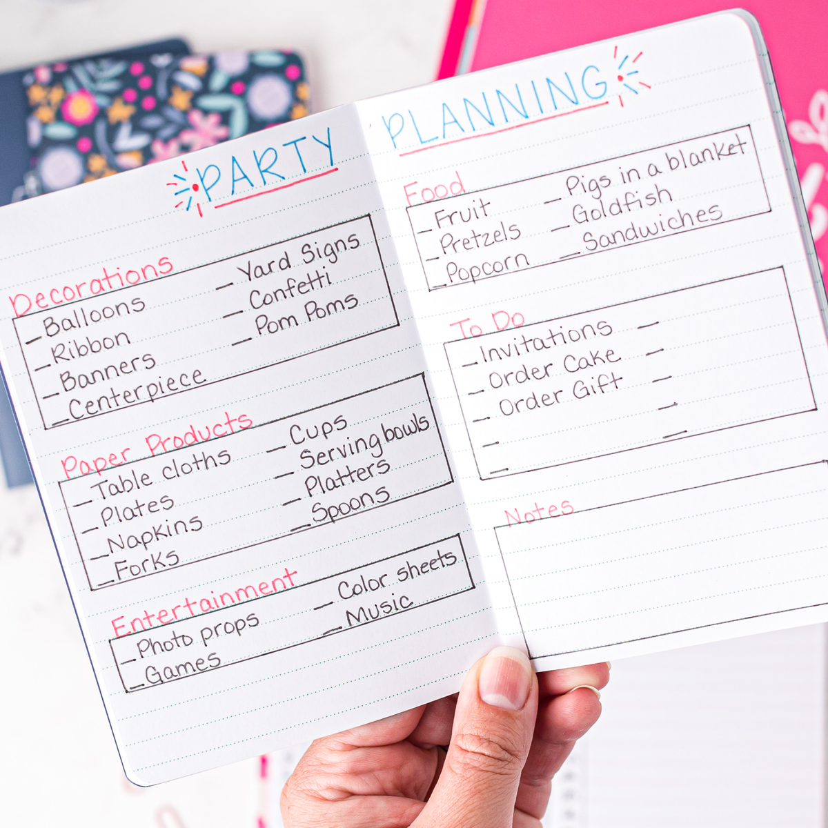Hand holding a mini notebook with party planning checklist on a white background