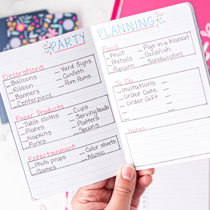 Hand holding a mini notebook with party planning checklist on a white background