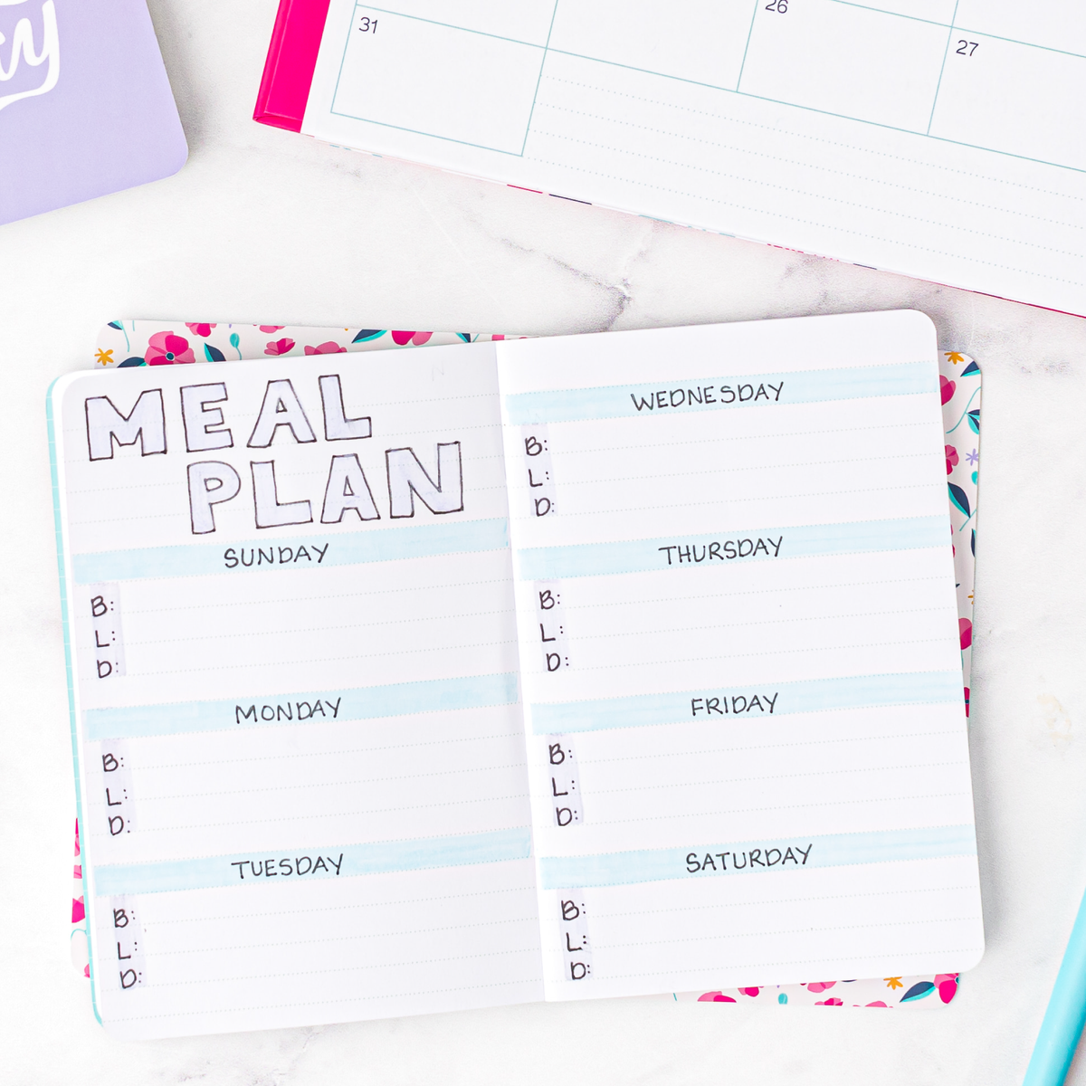 A meal plan drawn on a mini notebook  with a colorful border on a white surface