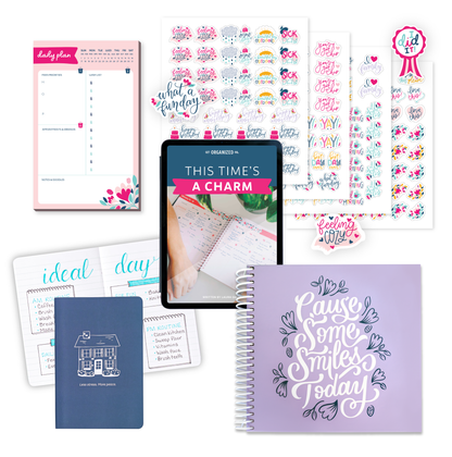 The lavender planner, a navy mini notebook that says "Less stress. More peace.", a tablet with the digital This Time's a Charm Guide on it, a daily planning notepad, and the decorative sticker pack.
