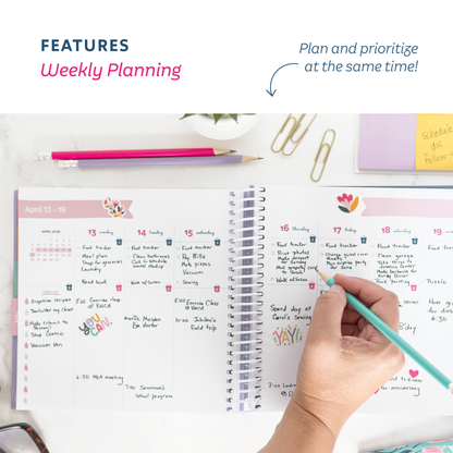 Weekly planning pages that allow you to prioritize and plane at the same time, with a hand holding a pen, surrounded by stationery items on a white surface.