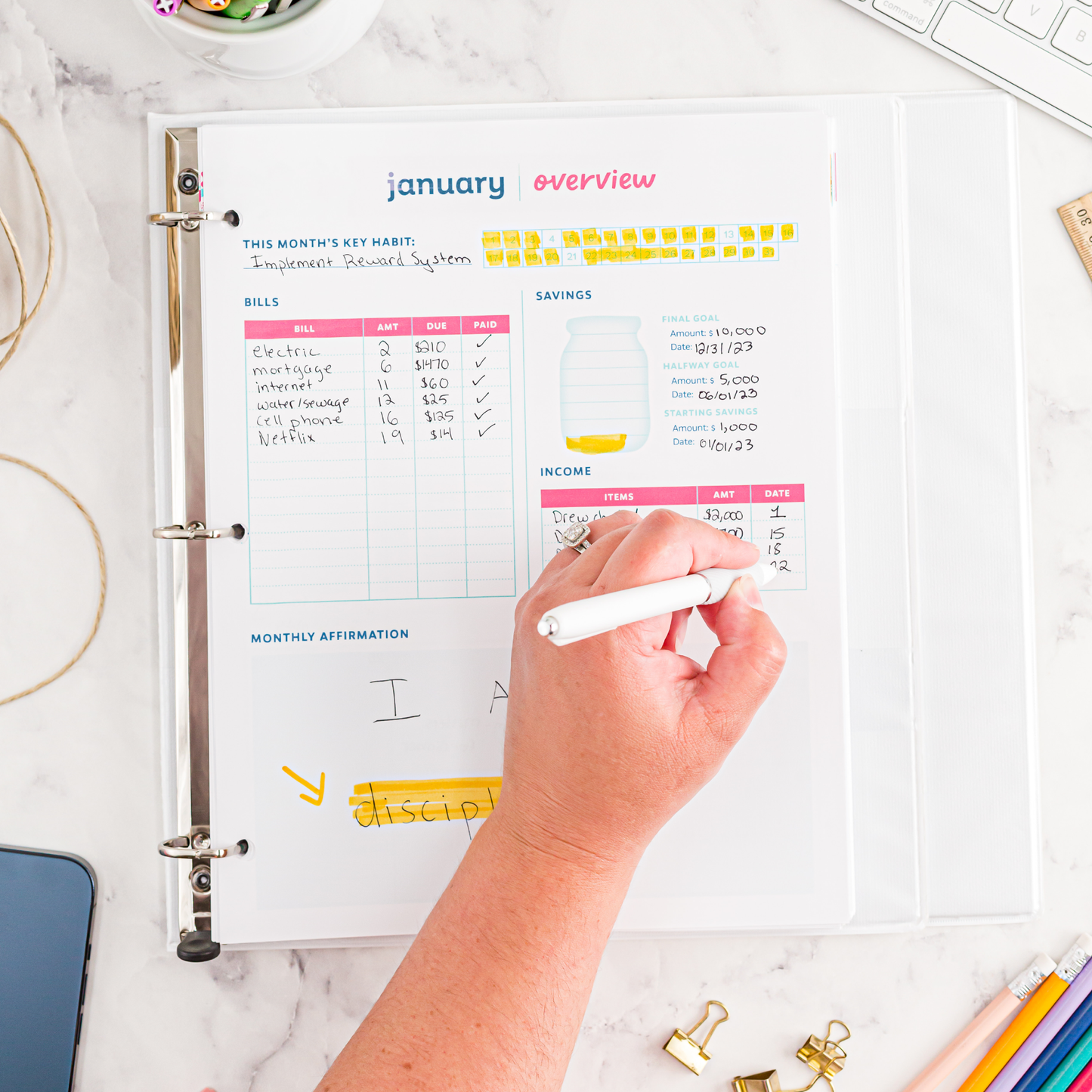 Person holding a pen on a marble surface, filling out a January Overview page.