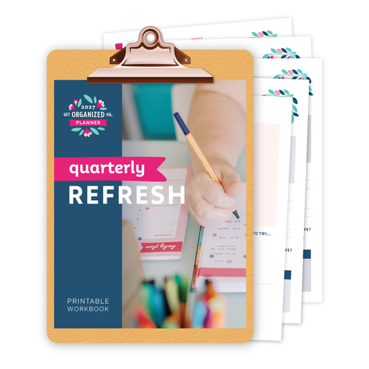 Clipboard with a printed 2027 Get Organized HQ Planner Quarterly Refresh Printable Workbook on it and scattered behind it.